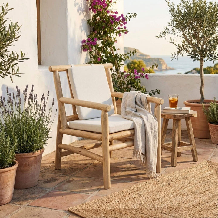 Akasa teak branch dining chair with white cushion and gray blanket on a patio with plants and a view of the sea.