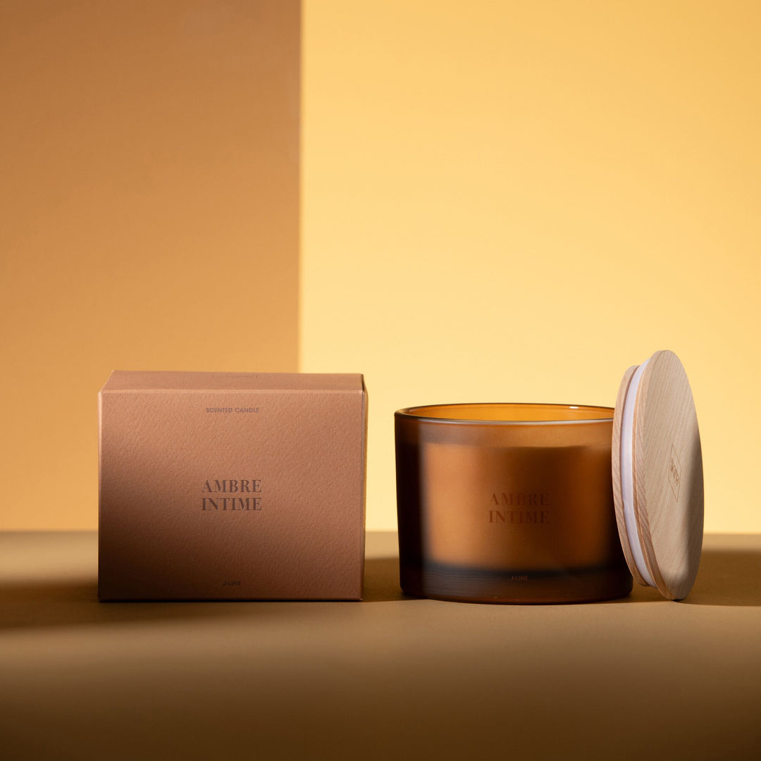 Small Amber Intime candle displayed beside its box on a warm-toned surface.