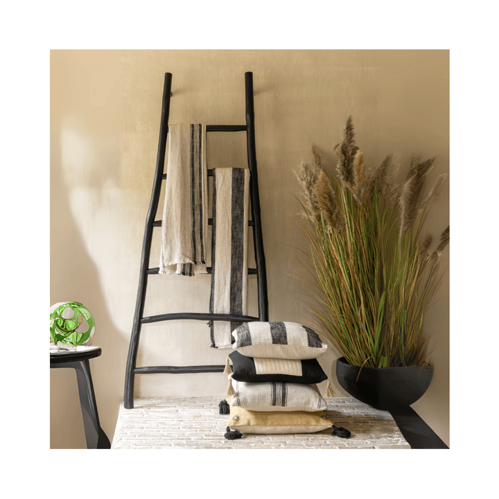 Aride black teak ladder styled with textiles and cushions in a modern interior.