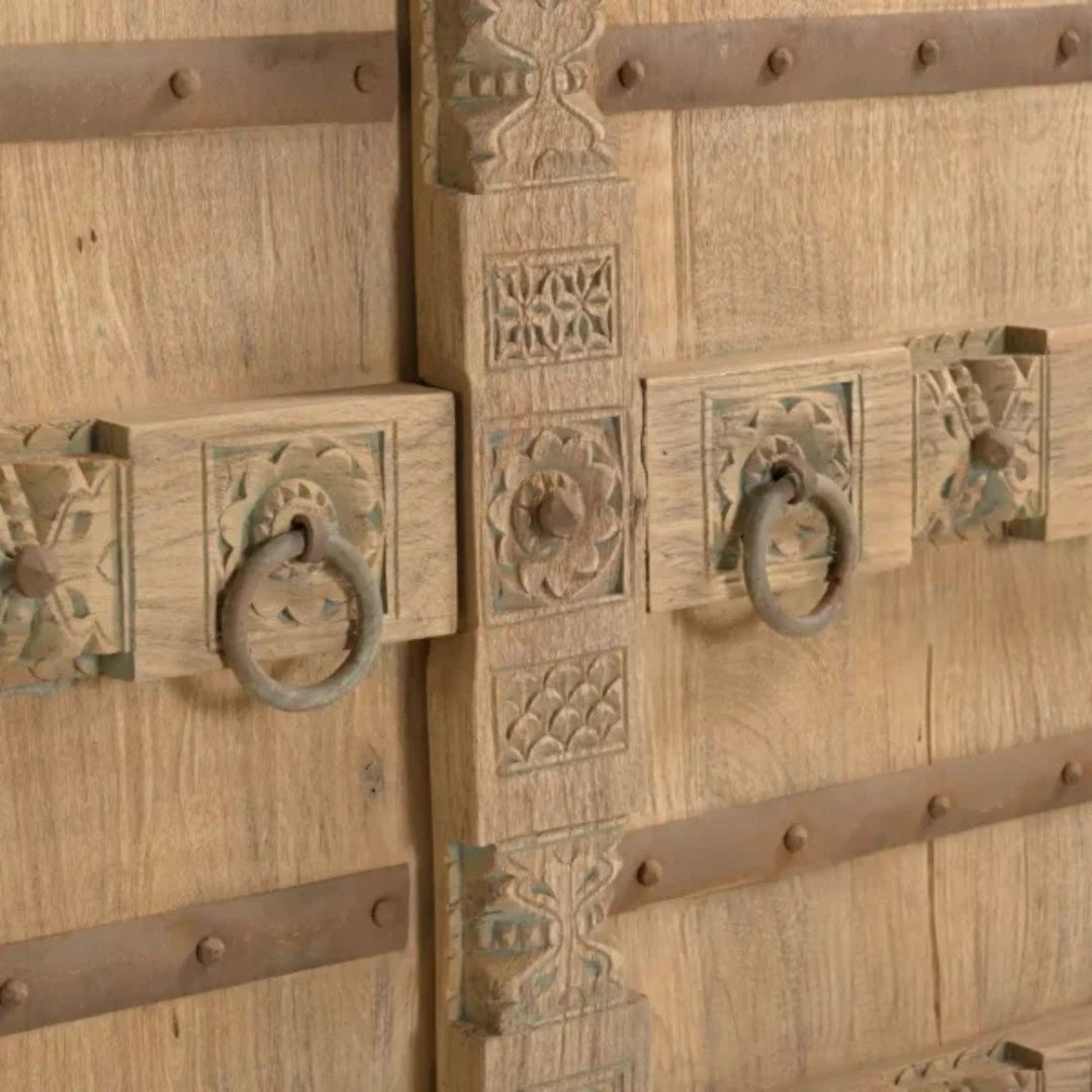 Close-up detail of the door hardware and carved-inspired panel showing the aged metal accents and natural wood texture.