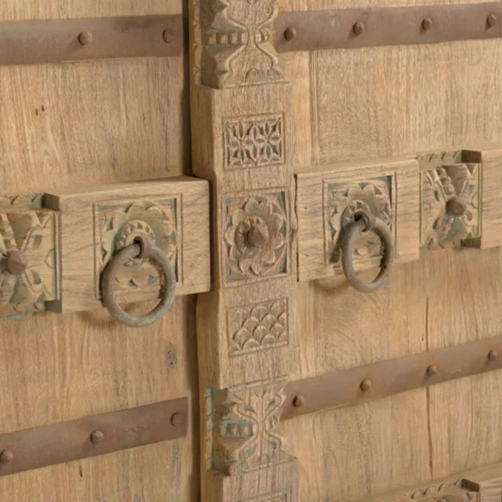 Close-up detail of the door hardware and carved-inspired panel showing the aged metal accents and natural wood texture.