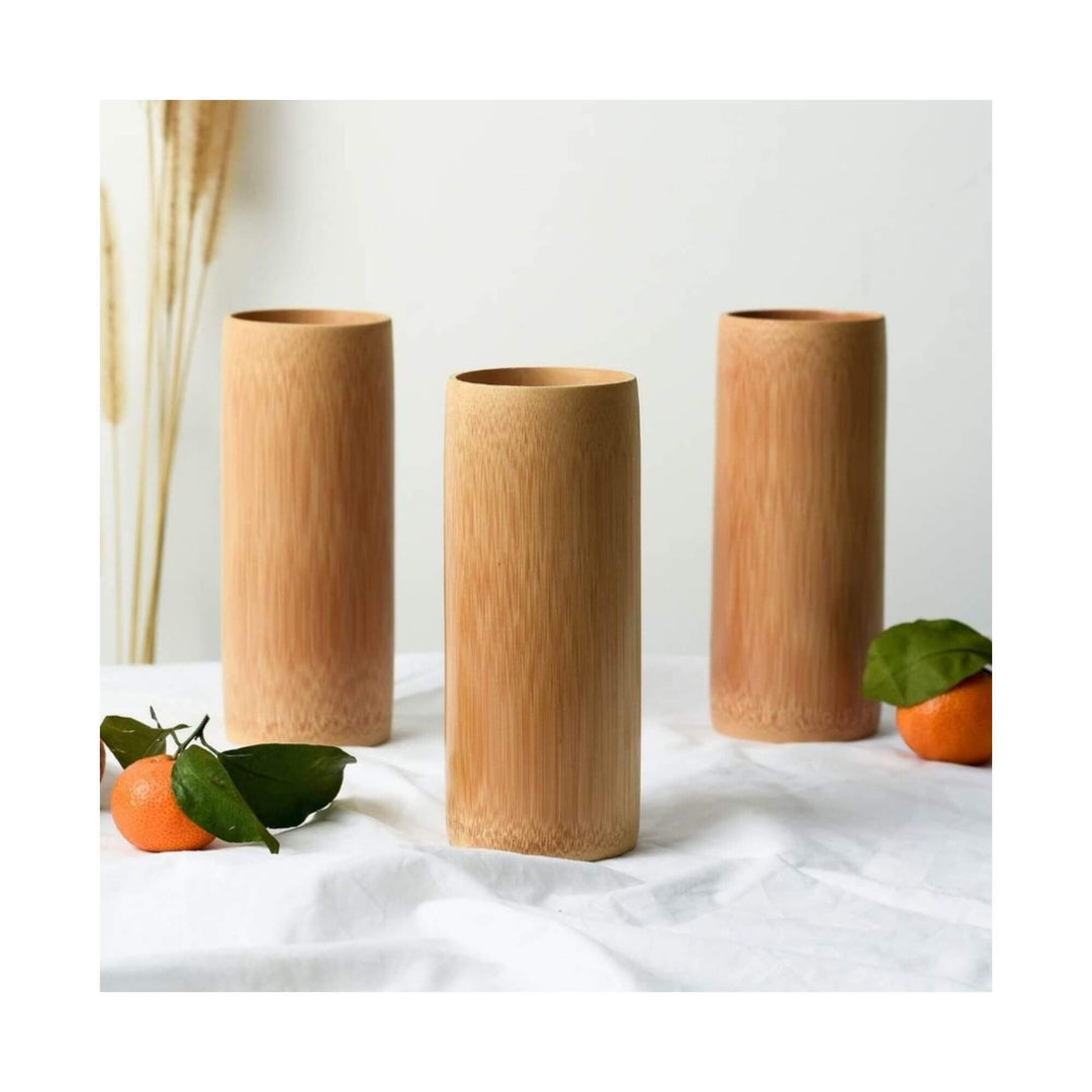 Three tall natural bamboo cups displayed on a white table with fresh mandarins.