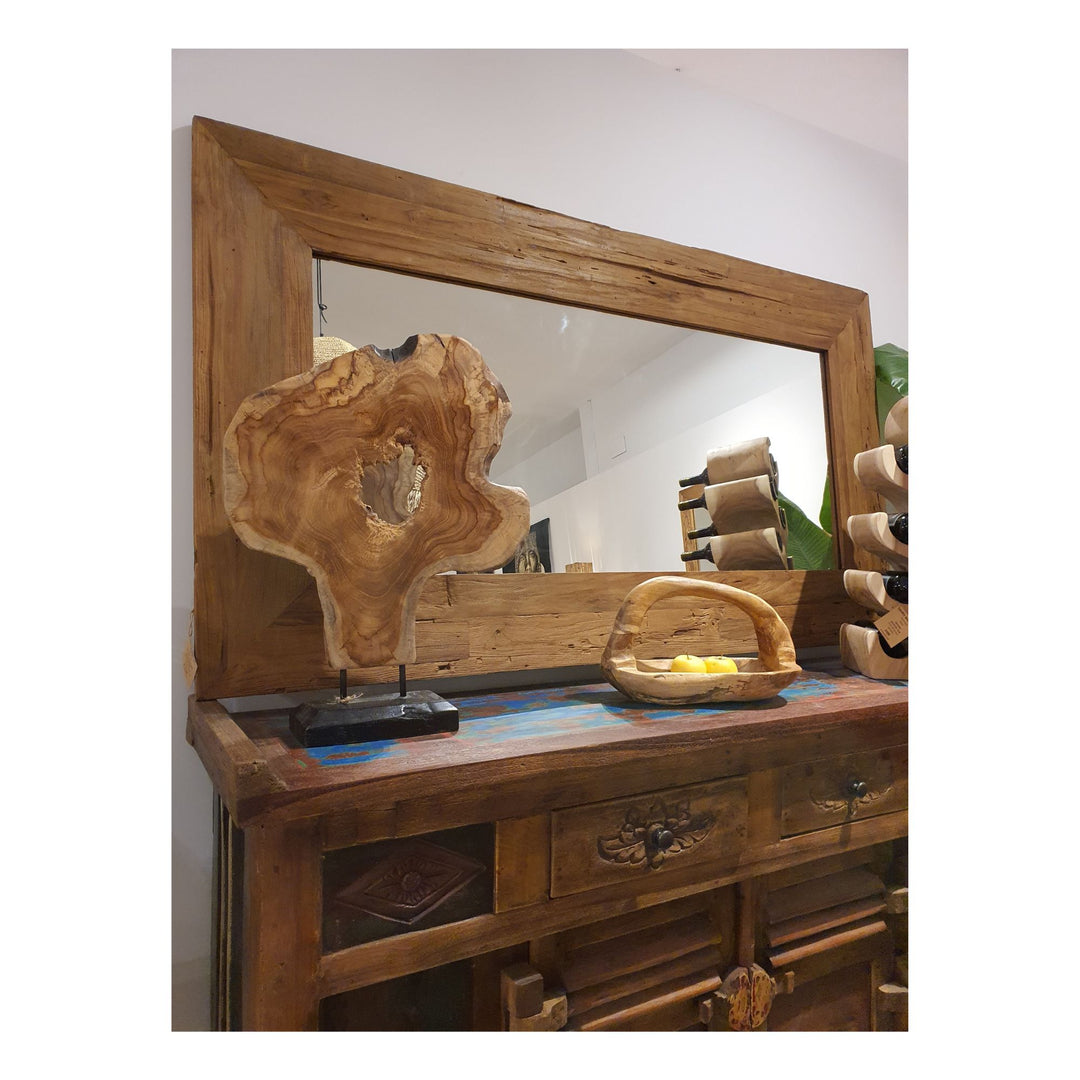 Teak figure stand on a dark sideboard in front of a wide wooden-framed mirror