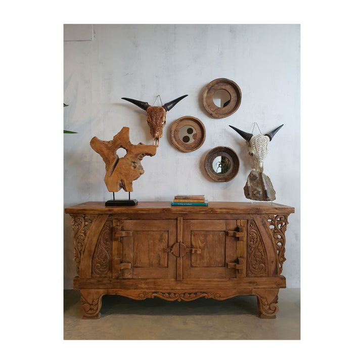 Batu Hiu teak figure stands styled on an ornate carved sideboard with wall decor in a living space.