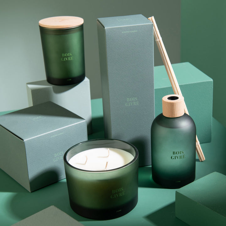 Lifestyle setup featuring the Bois Givré candle collection arranged on green-toned blocks.