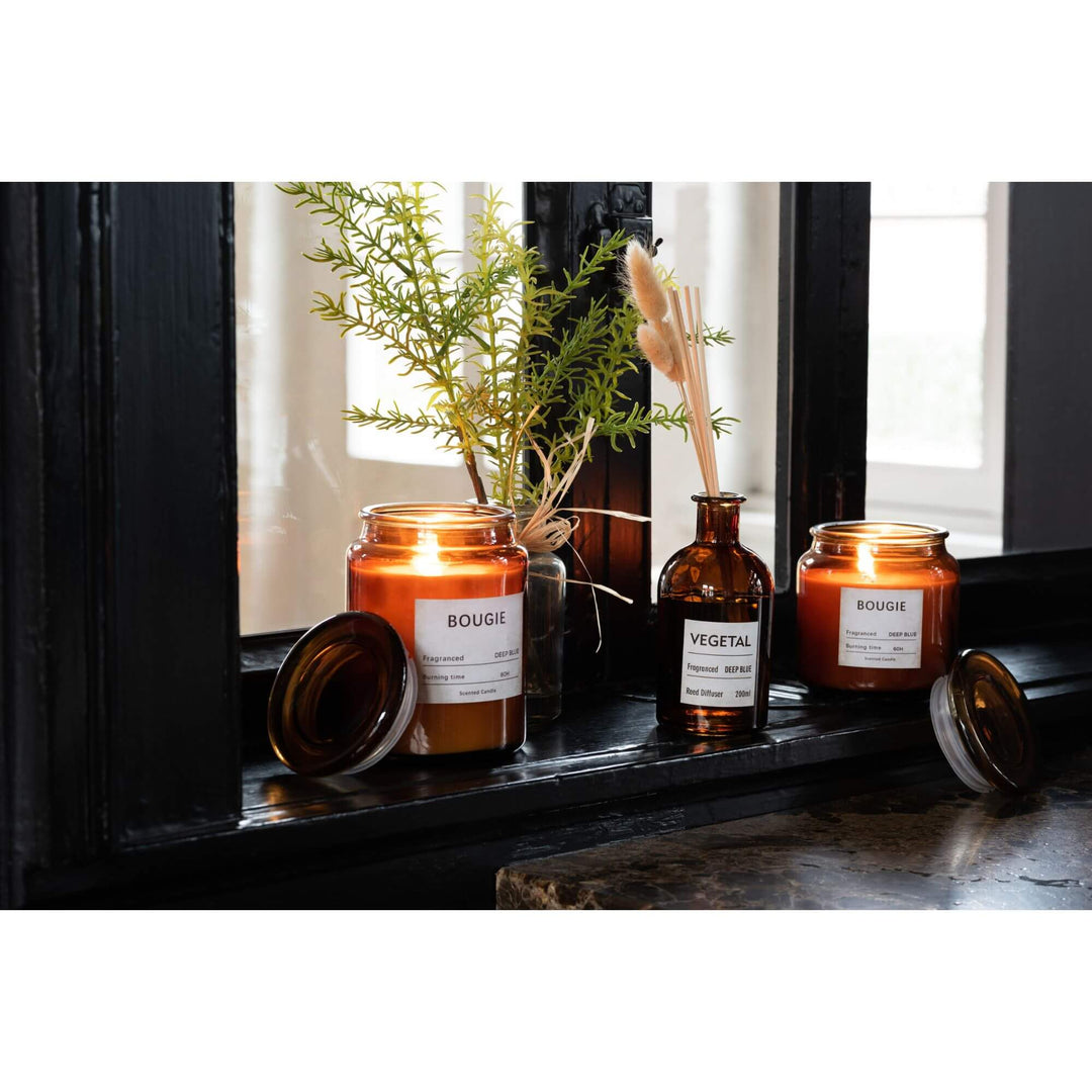 Bougie Small Candle lit on a dark windowsill with amber glass jar and Deep Blue fragrance label.