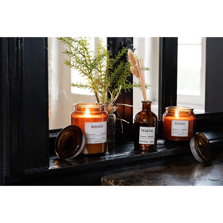 Bougie Small Candle lit on a dark windowsill with amber glass jar and Deep Blue fragrance label.