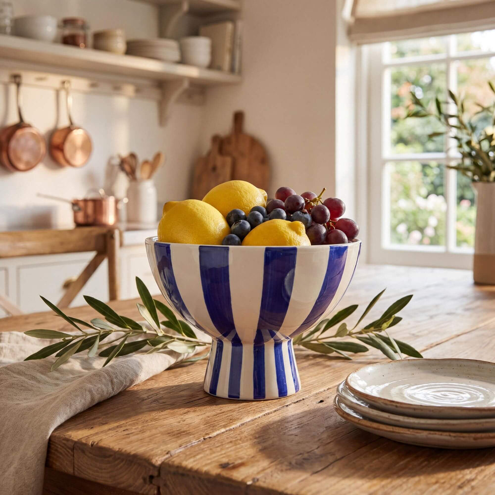 Styled kitchen setting featuring the Capri pedestal bowl displayed with fruit on a wooden table.