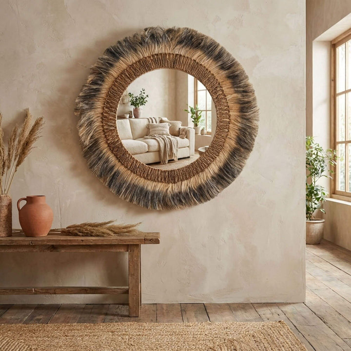 Round woven Cendana mirror on a wall with a wooden bench and decor items in a room.
