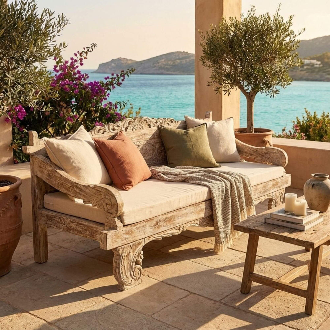 Outdoor seating area with a Chloe indonesian carved teak wood daybed, cushions, and a small table by the sea.