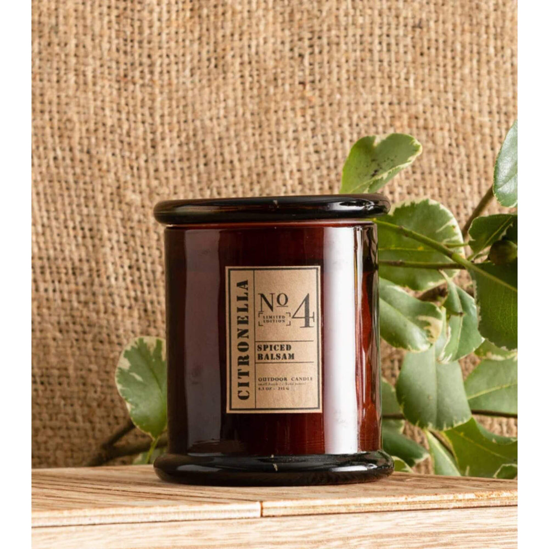 Citronella candle in amber glass jar placed on wooden surface with natural background