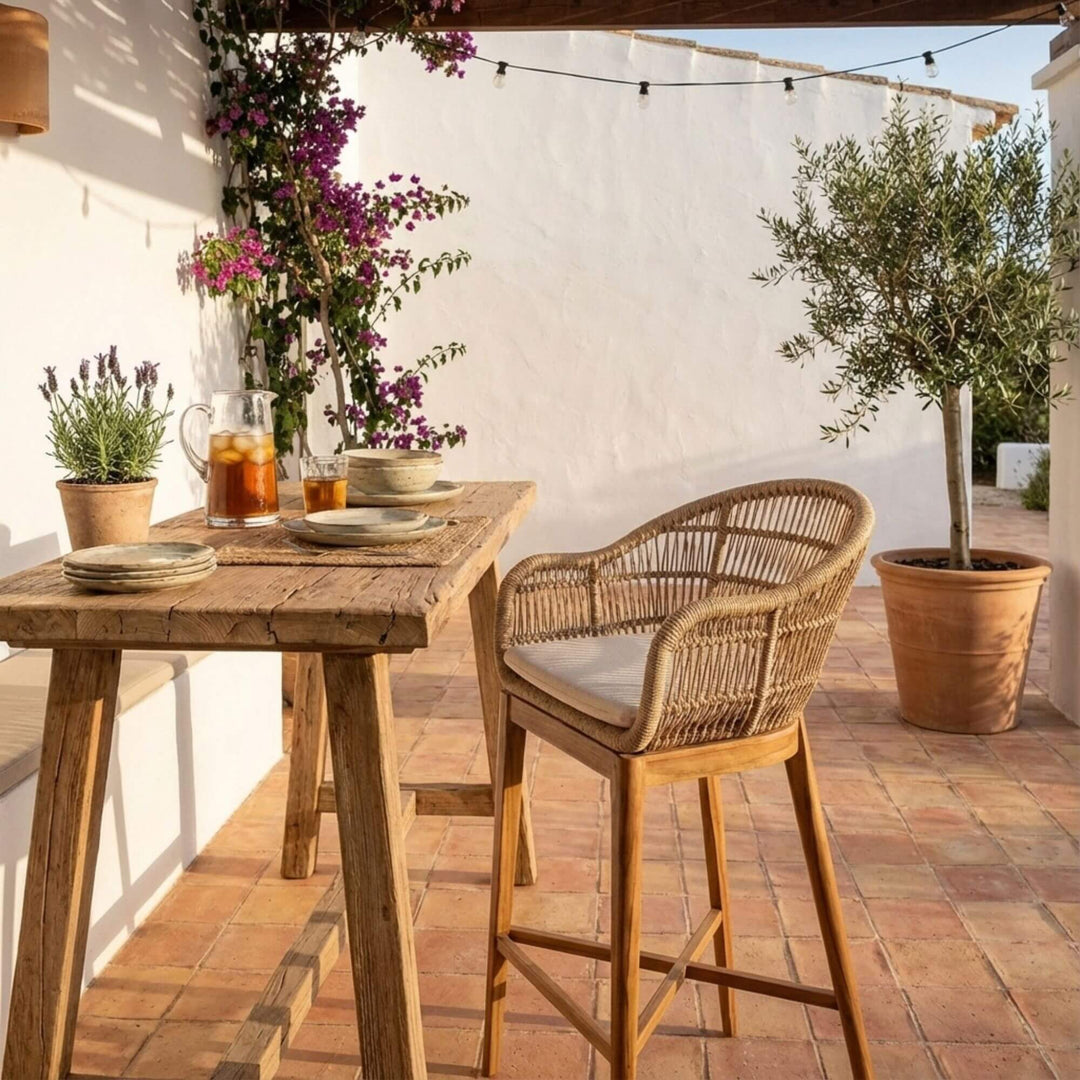 Outdoor setting with wooden table and Coco Bar stool on a patio, featuring potted plants and flowers.