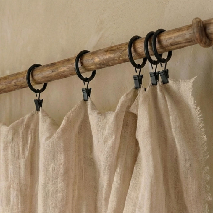 Curtain rings installed on a wooden curtain rod holding a lightweight linen curtain.