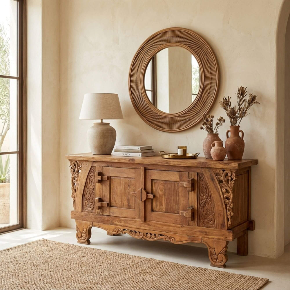 Dalia carved teak wood buffet with decorative items in a room with a large mirror and window.