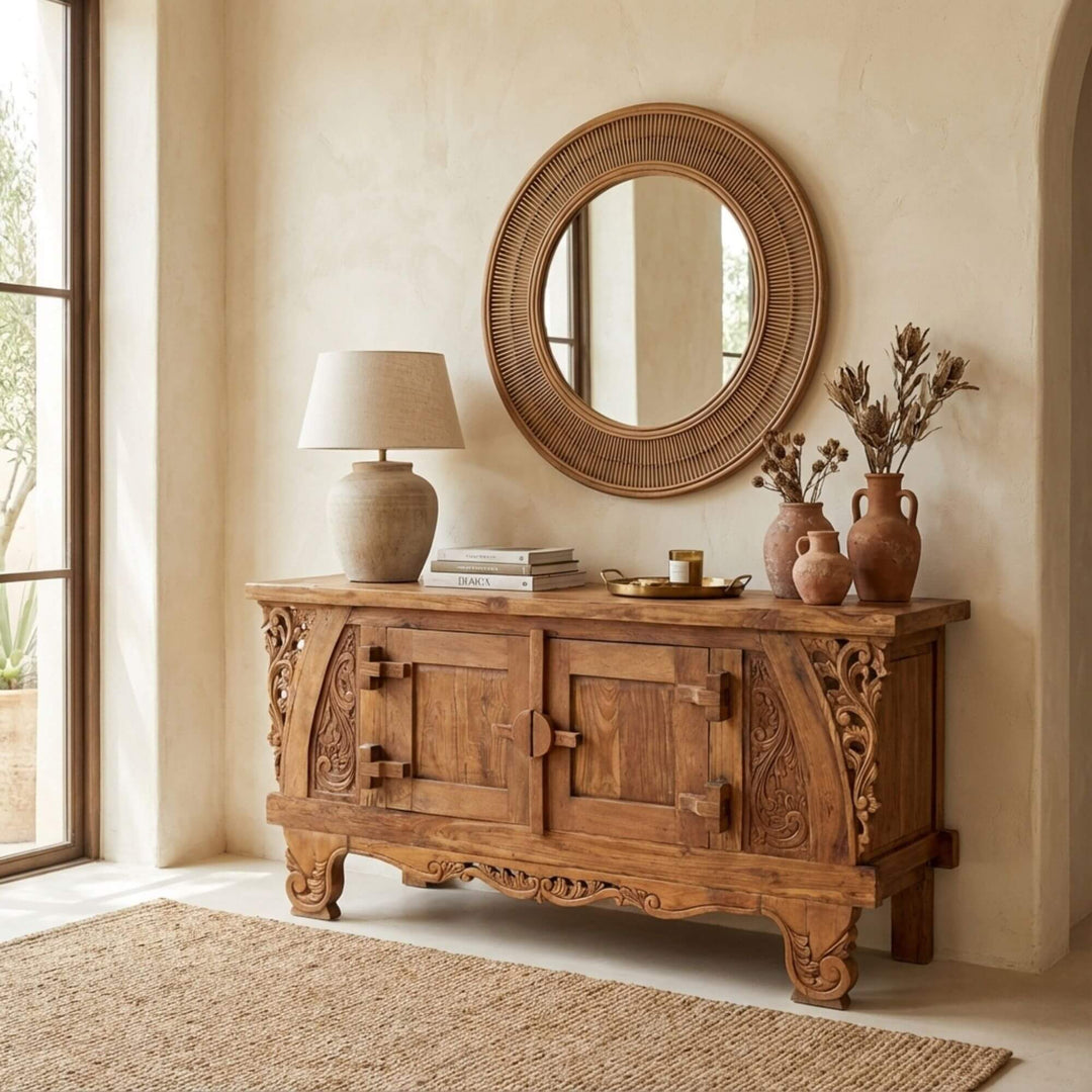 Dalia carved teak wood buffet with decorative items in a room with a large mirror and window.