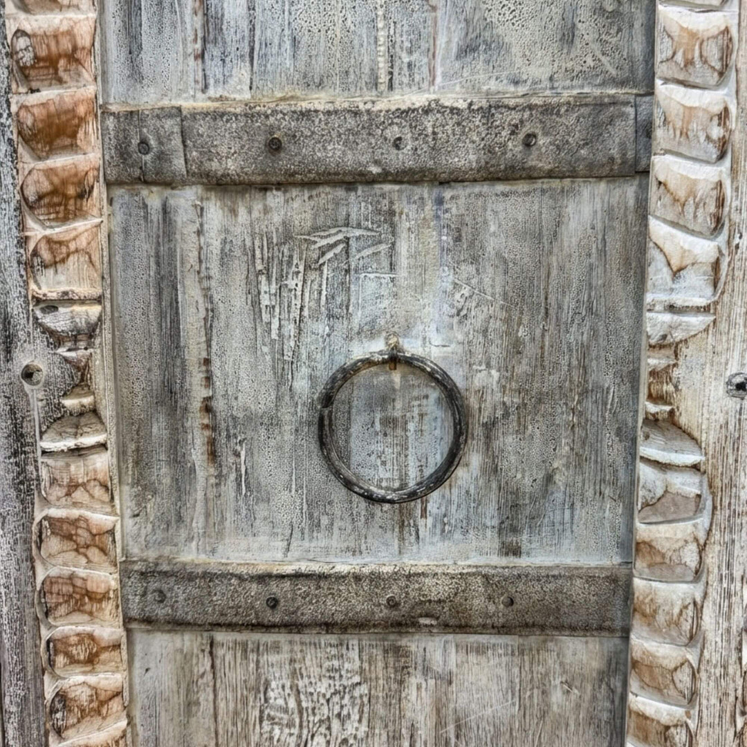 Close-up of the carved wooden door with antique ring handle and distressed texture.