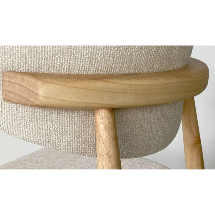 Close-up detail of the chair showing the soft beige fabric upholstery and smooth natural wood arm detail.