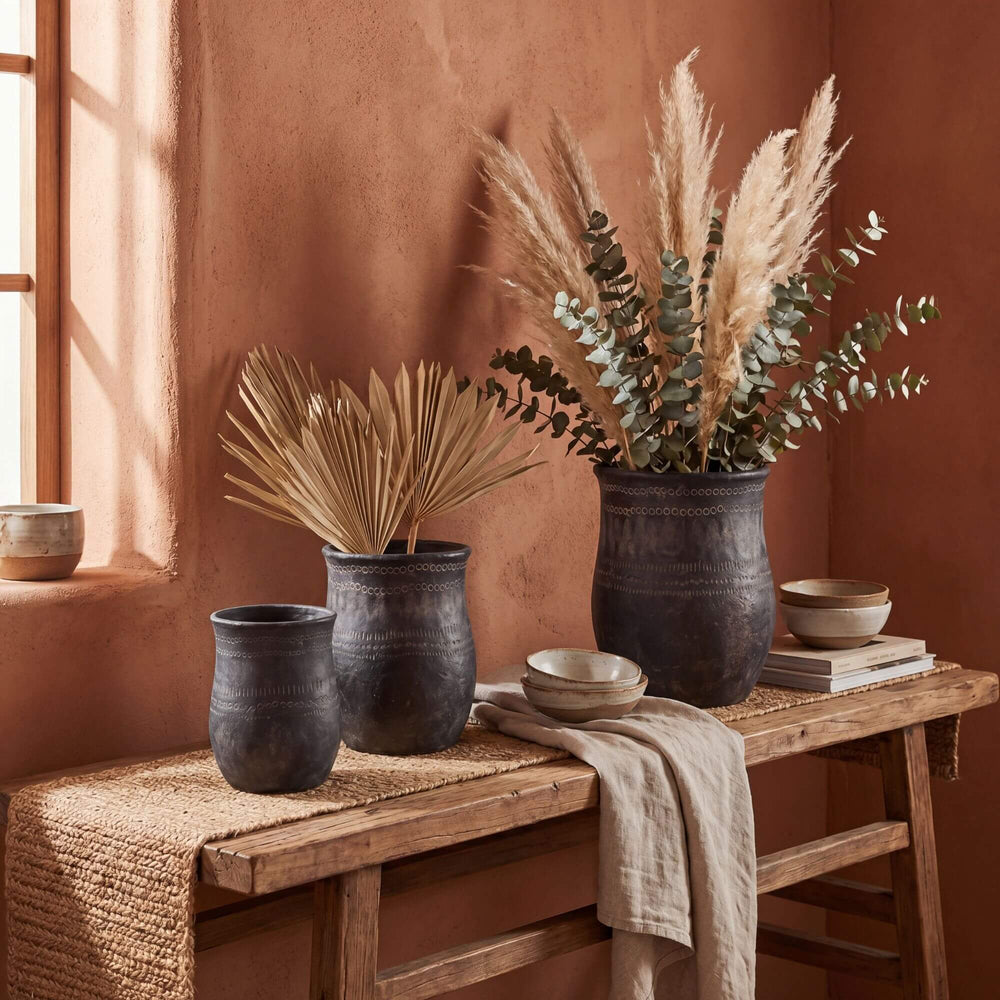 Styled interior setting featuring etched black planters arranged on a wooden console with dried foliage.