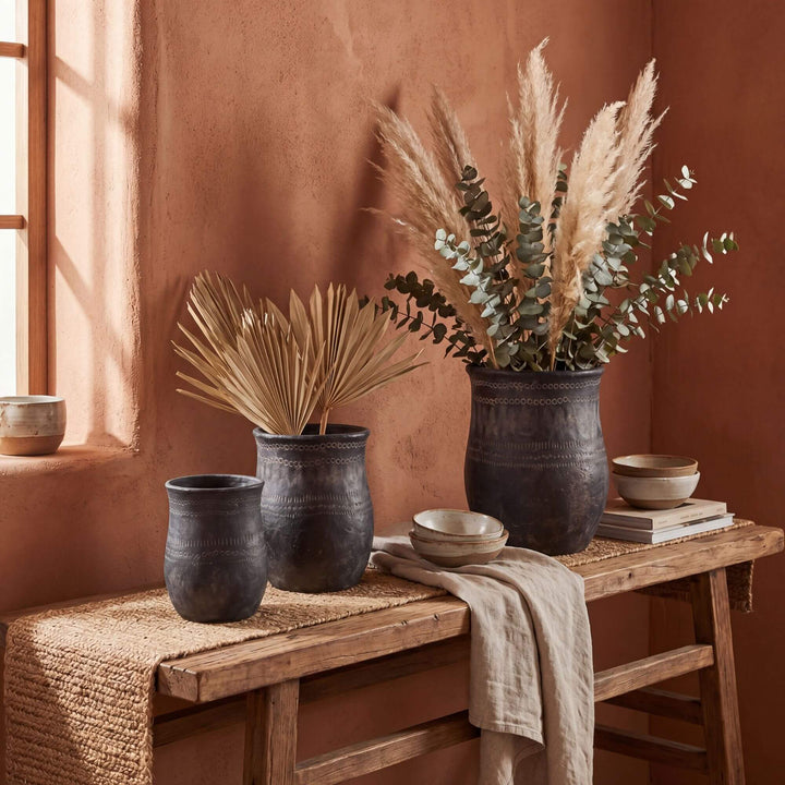 Styled interior setting featuring etched black planters arranged on a wooden console with dried foliage.