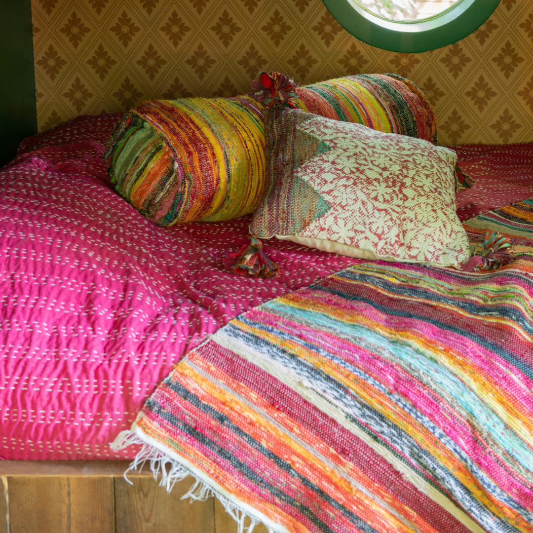 Farsha chindi bolster cushion styled on a bed with vibrant ethnic textiles