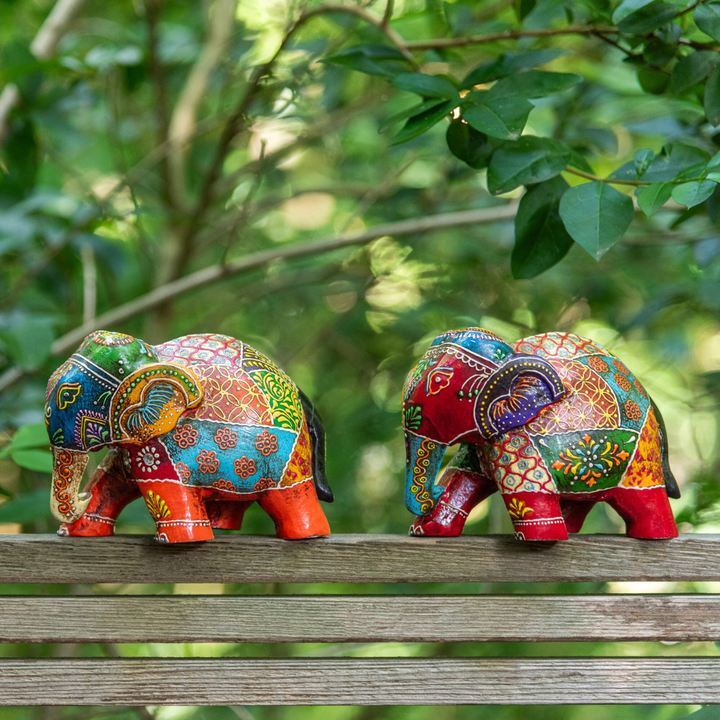 Colorful wooden elephant figures displayed outdoors on a wooden surface surrounded by greenery.