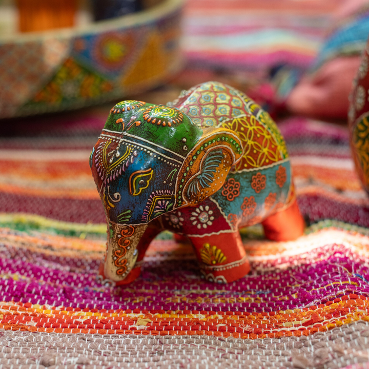 Close-up of a multicolor hand-painted wooden elephant figure on a textured fabric surface.