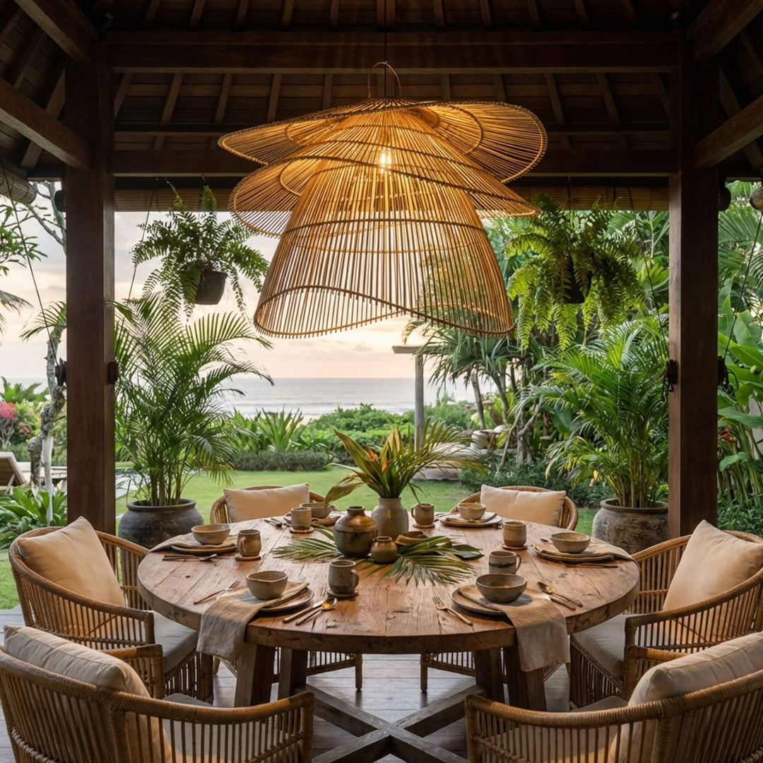 Outdoor dining setup with a Flamenco ceiling lamp,  wooden table and chairs under a thatched roof, surrounded by lush greenery.