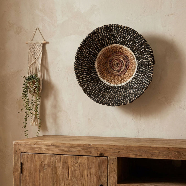 Woven Harum wall deco art piece on a textured wall above a wooden cabinet.
