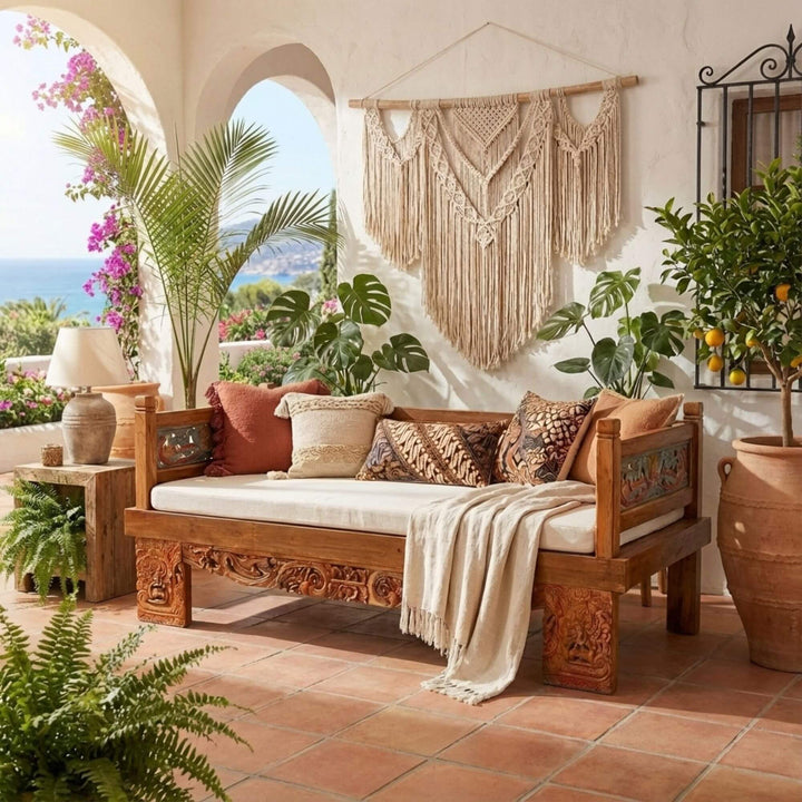Hemera Indonesian carved teak wood daybed with decorative pillows and a macrame wall hanging in a garden setting.