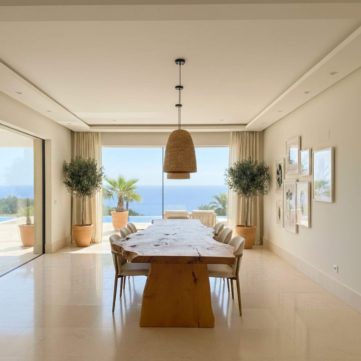 Modern dining room with a large Hera Dining table and chairs, featuring a scenic view of the ocean through large windows.