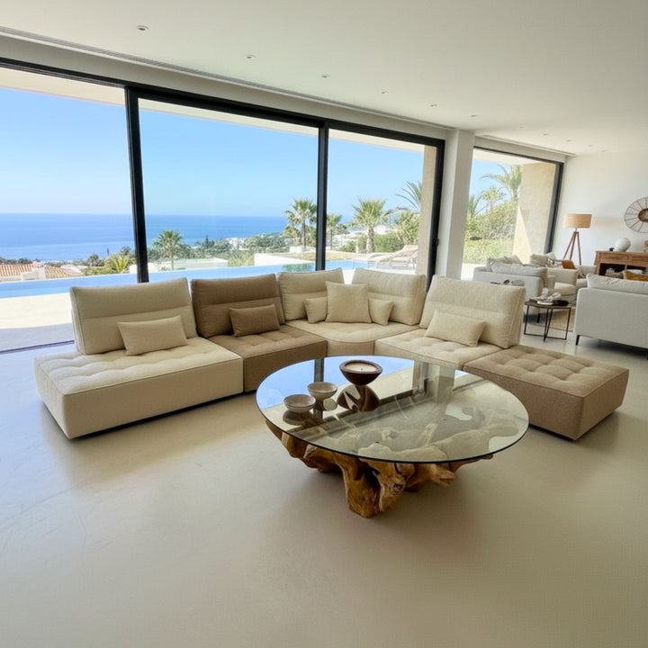 Large corner setup of the Hera Modular Sofa in cream cotton facing a coffee table with sea views.