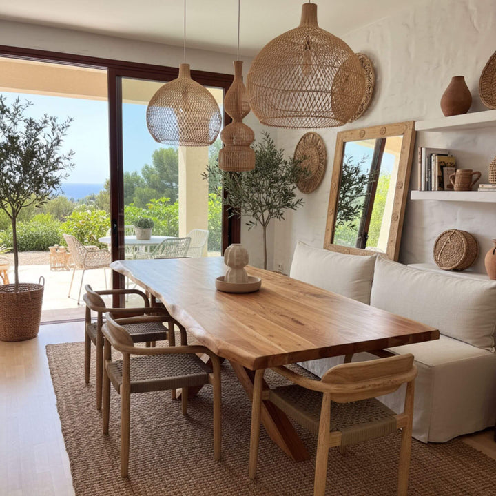 Dining area with wooden Lea dining table and chairs, wicker pendant lights, and a view of the outdoors.