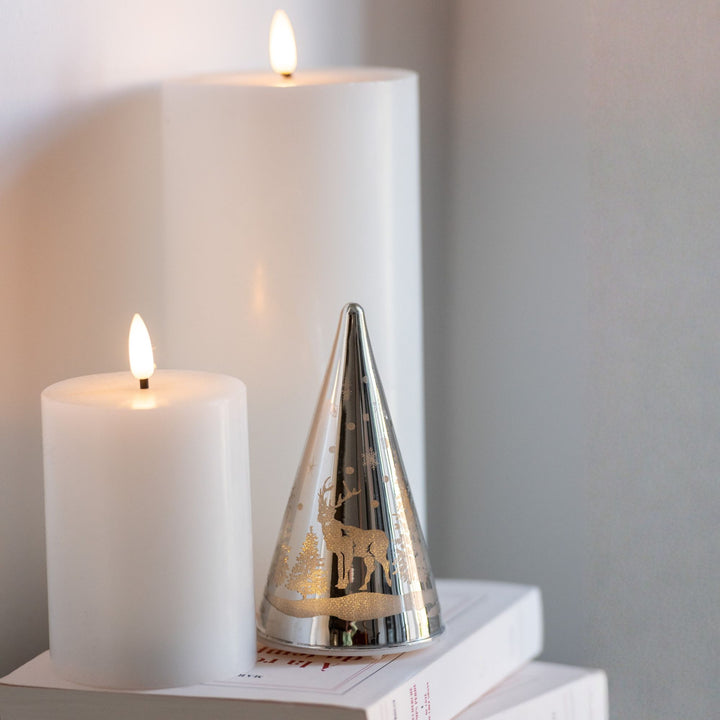 Decorative silver cone with cut-out designs on a stack of books next to two Led white candles.