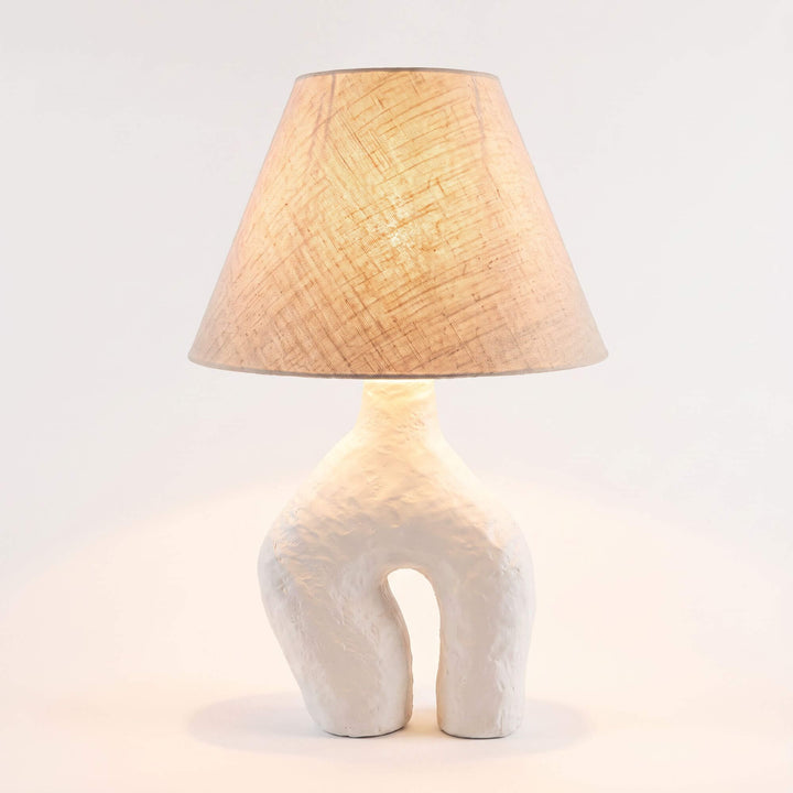 Legy table lamp illuminated with a natural linen shade and sculptural papier-mâché base