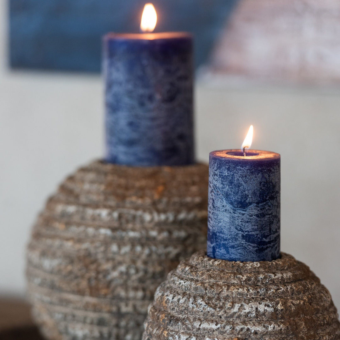 Styled scene featuring Mahé Blue Outdoor Candles lit on outdoor décor pieces.