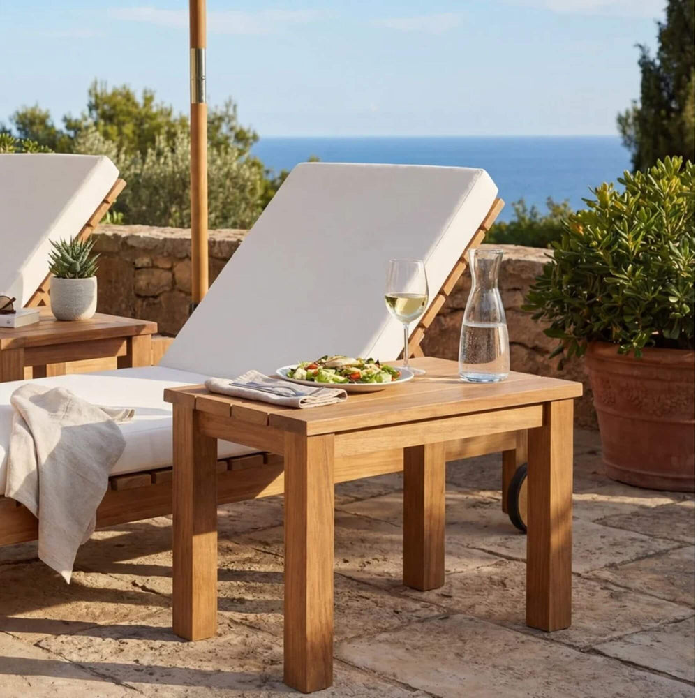 Styled outdoor terrace setting featuring the Maldives side table beside sun loungers with a sea view.