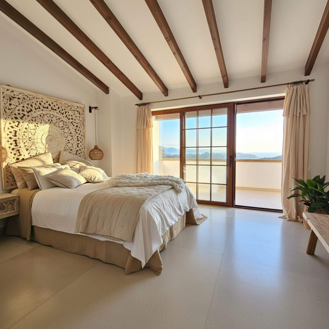 Beach-style bedroom with wooden beams, a bed with beige and white bedding, and a sliding glass door leading to a balcony.