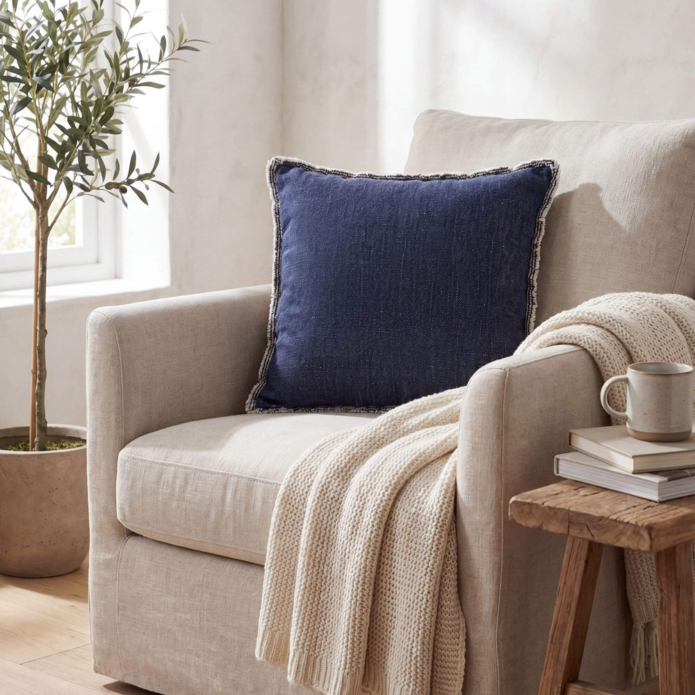 Styled interior setting featuring the Midnight Blue fringed cushion on an armchair with warm natural textiles.