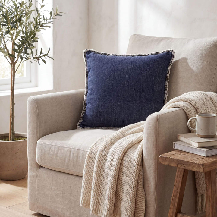 Styled interior setting featuring the Midnight Blue fringed cushion on an armchair with warm natural textiles.