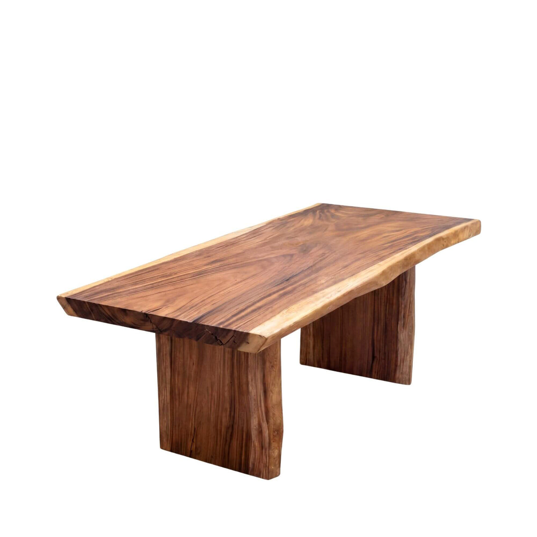 Front angled view of the Motu Nui suar wood dining table showing its thick solid wood top and sculptural panel legs.