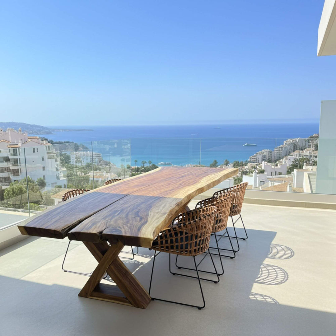 Motu nui suar wood dining table with chairs on a balcony overlooking the ocean.