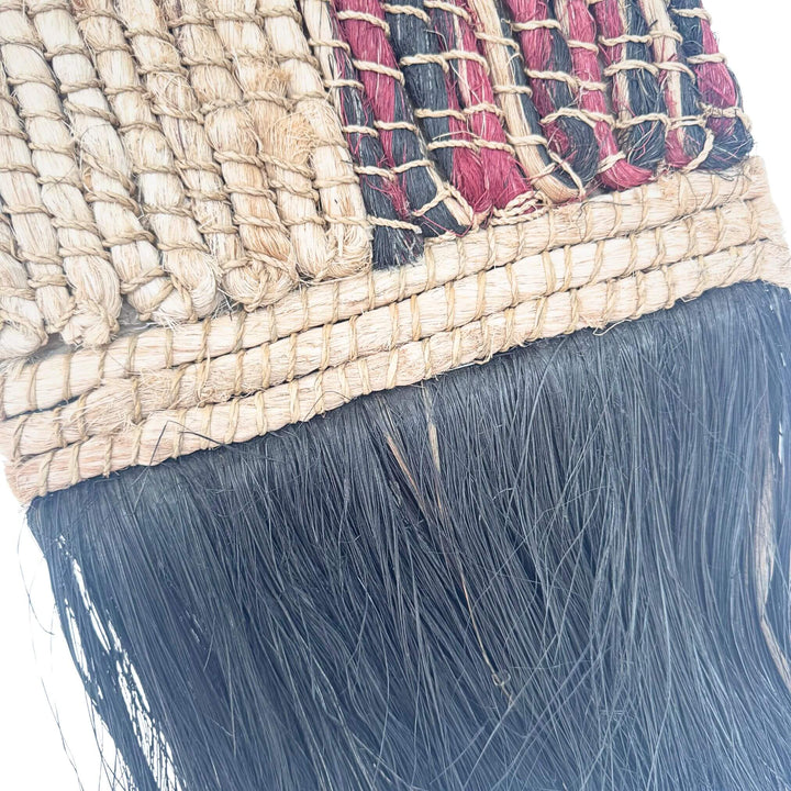 Close-up of Merak Wall Deco handwoven from abaca, rattan, and cotton with natural and black patchwork design and fringe