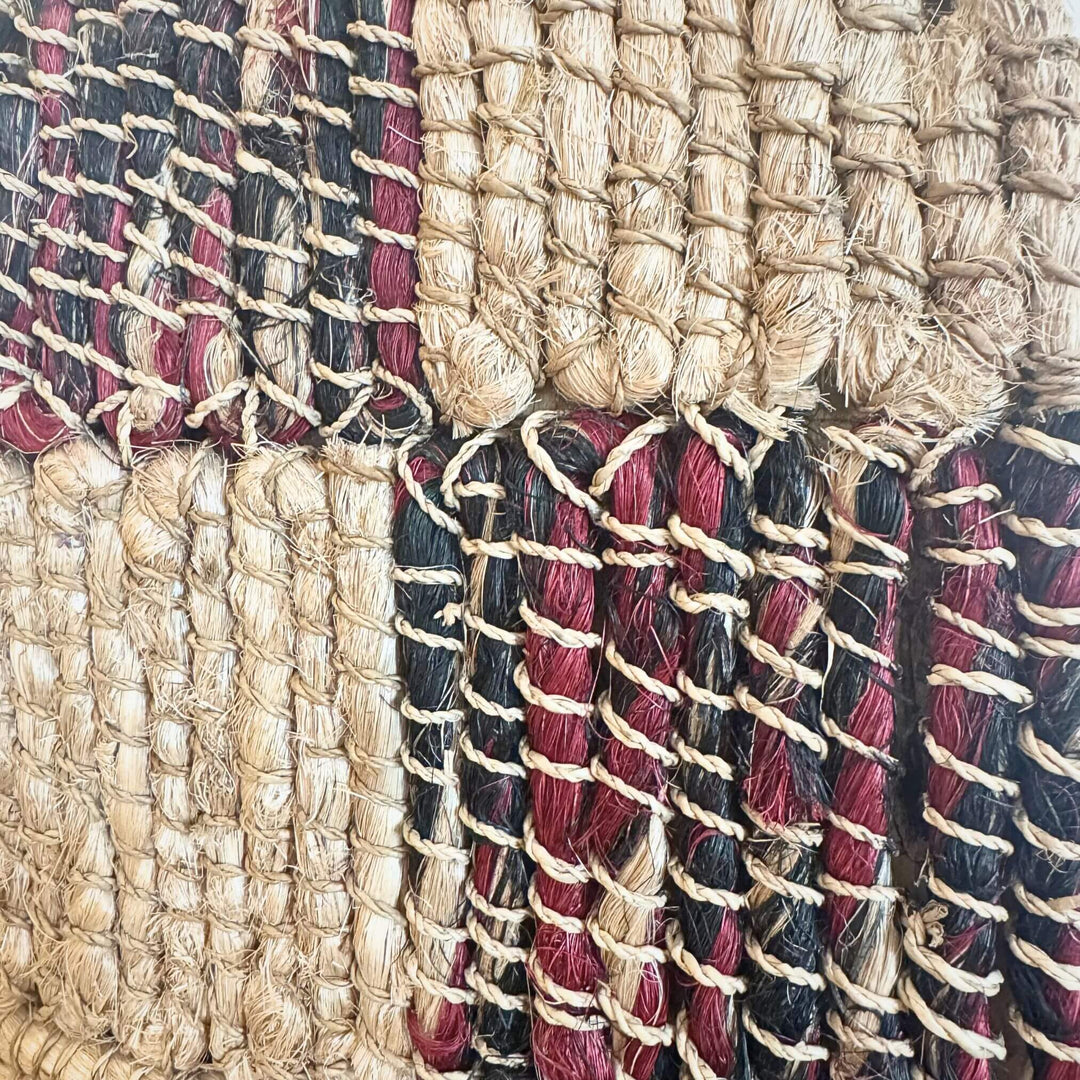 Close-up of Merak Wall Deco handwoven from abaca, rattan, and cotton with natural and black patchwork design and fringe