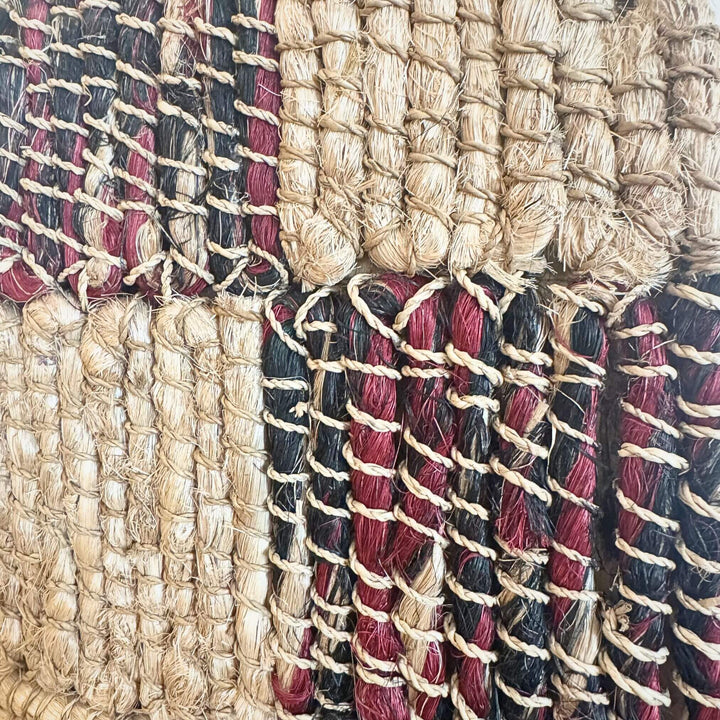 Close-up of Merak Wall Deco handwoven from abaca, rattan, and cotton with natural and black patchwork design and fringe