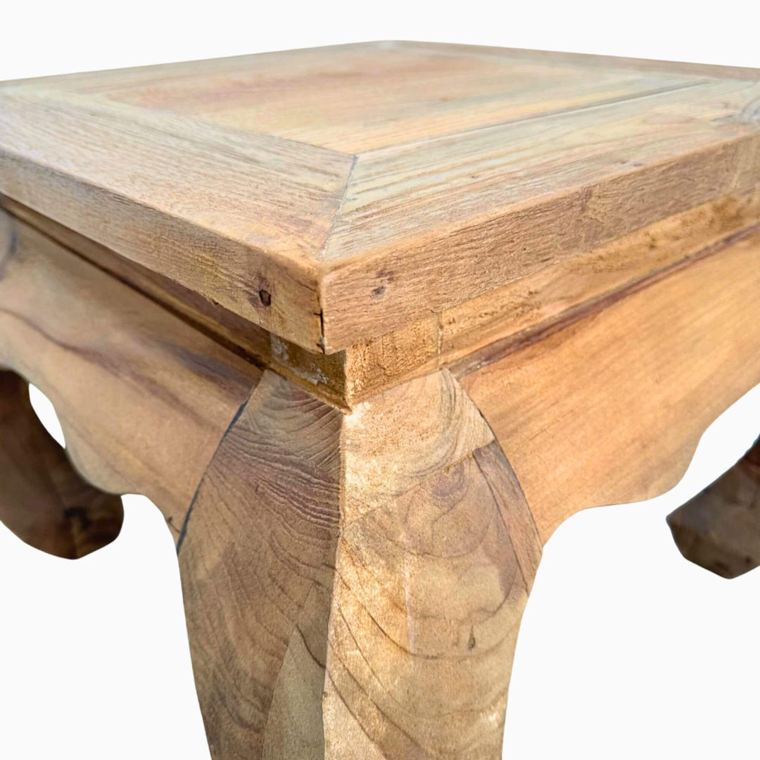 Close-up of the teak Opium Table showing curved leg detail and wood grain.
