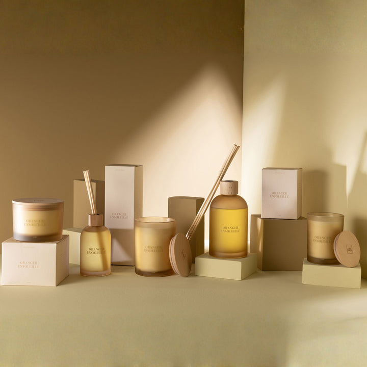 Group display of Oranger Ensoleillé diffusers and candles on a styled tabletop.