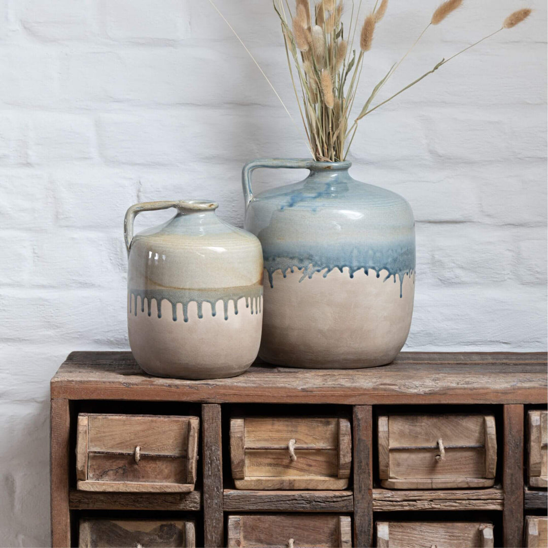 Two ceramic jars with a textured finish on a wooden Otto Drawer against a light brick wall.