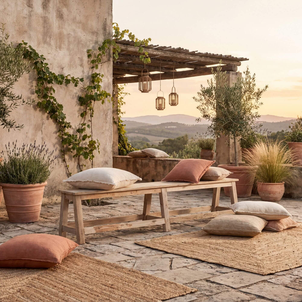 Outdoor patio with Reethi teak wood bench, cushions, and potted plants against a scenic backdrop.
