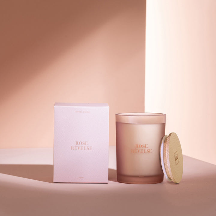 Styled image of the Rose Rêveuse candle beside its box in a warm, elegant setting.
