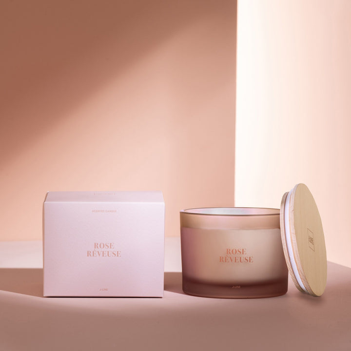 Styled image of the Rose Rêveuse candle beside its box in a warm, elegant setting.